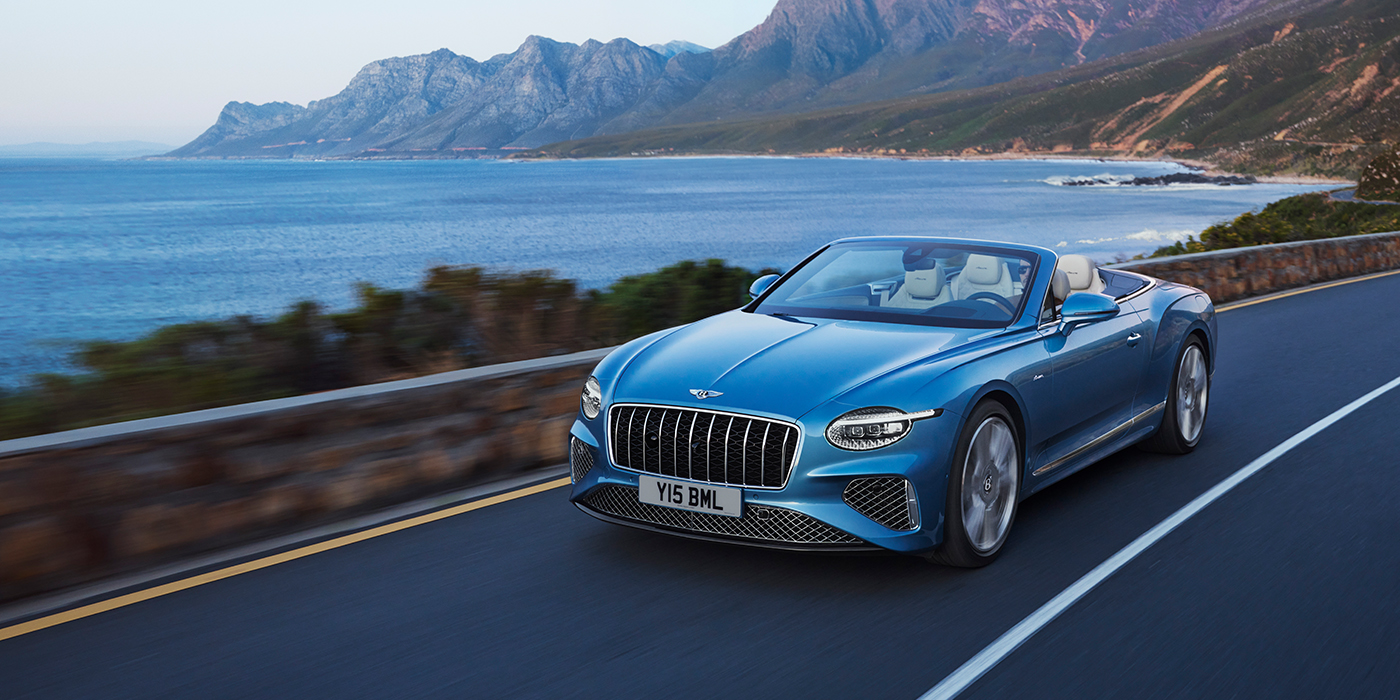 Bach Premium Cars GmbH New Bentley Continental GTC Azure convertible in Light Windsor blue paint with 22 inch Azure wheels and chrome grill, driving dynamically by the sea