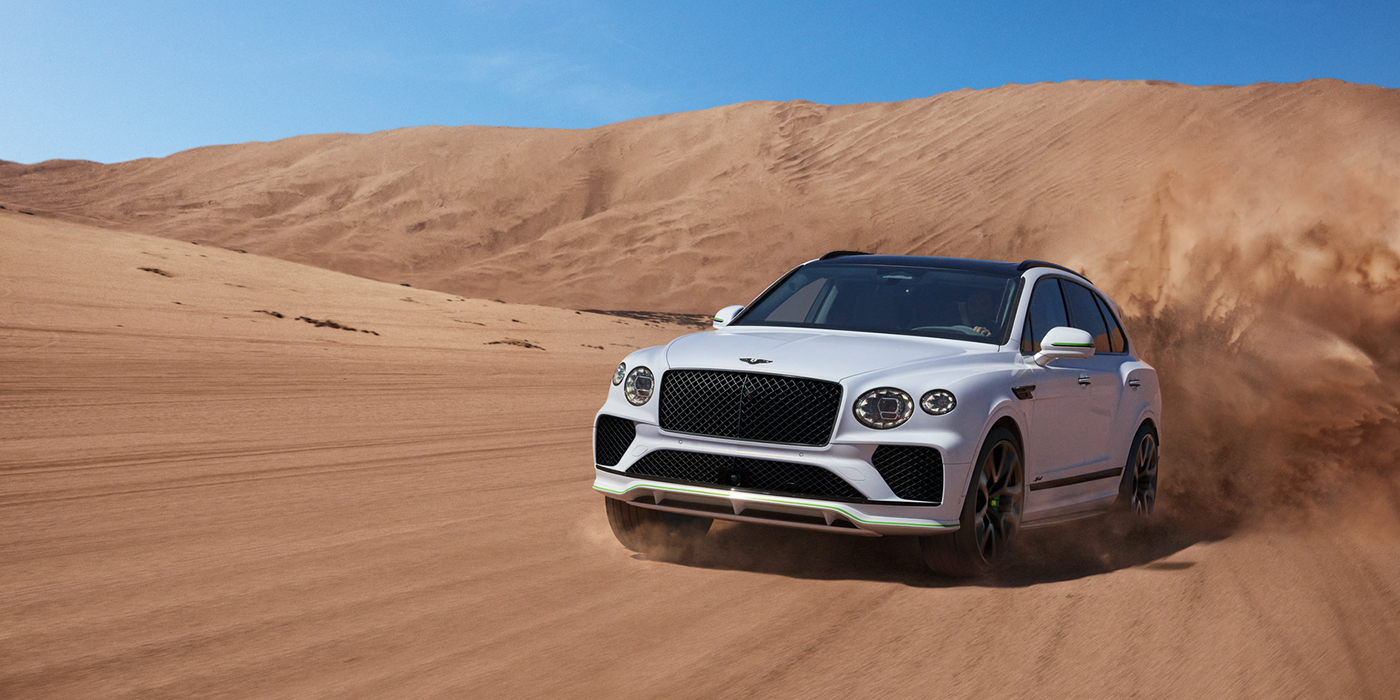 Bach Premium Cars GmbH Bentley Bentayga Speed SUV front three quarter in Snow Quarts Pearlescent by Mulliner white paint driving dynamically through the desert