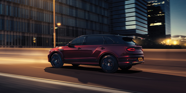Bach Premium Cars GmbH Bentley Bentayga Extended Wheelbase Mulliner SUV in Cricket Ball red paint driving dynamically in city at night