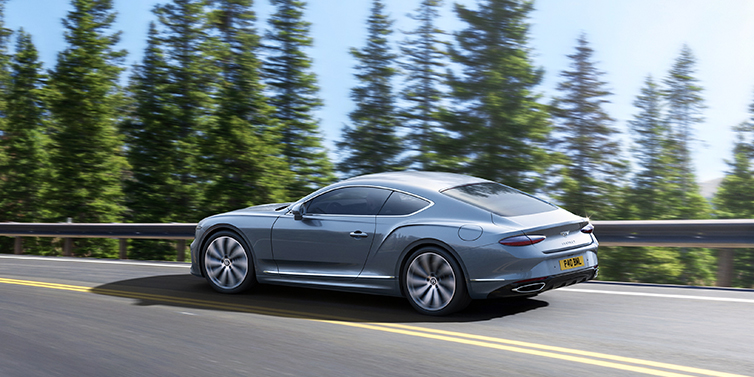 Bach Premium Cars GmbH New Bentley Continental GT coupe in Silverlake paint, seen from the rear, driving dynamically on a tree-lined road